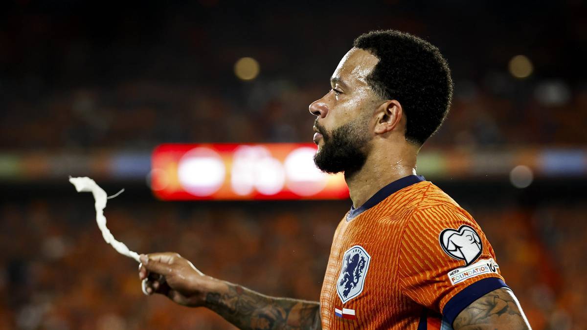 Piłkarz Memphis Depay w pomarańczowej koszulce z herbem Holandii, trzymający kawałek białej wstążki.