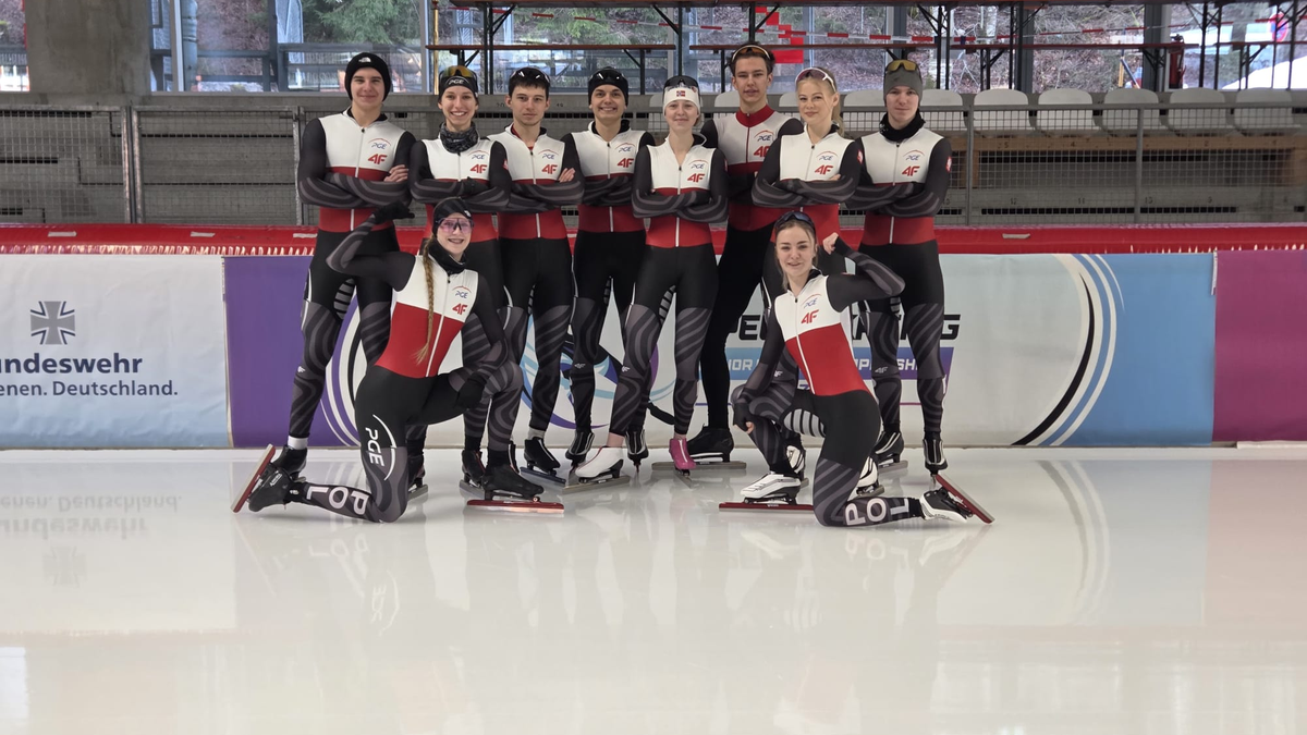 Grupa polskich łyżwiarzy szybkich junior&oacute;w w strojach reprezentacyjnych pozuje do zdjęcia na lodowisku przed zawodami.