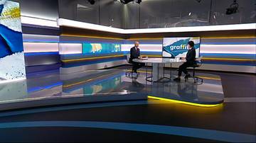 Dwoje prowadzących w nowoczesnym studio telewizyjnym siedzi przy okrągłym stole podczas nagrania programu.