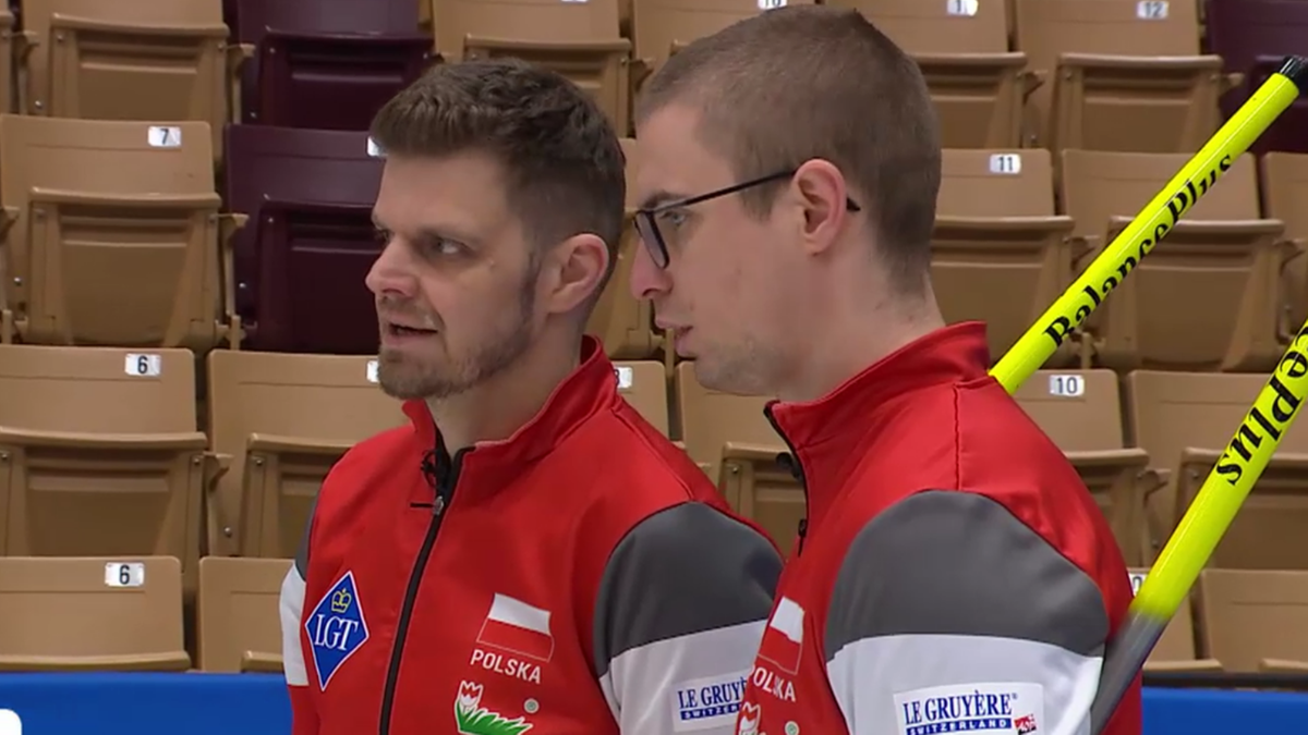 Dw&oacute;ch zawodnik&oacute;w curlingu reprezentacji Polski w czerwonych strojach sportowych z białymi i szarymi elementami.