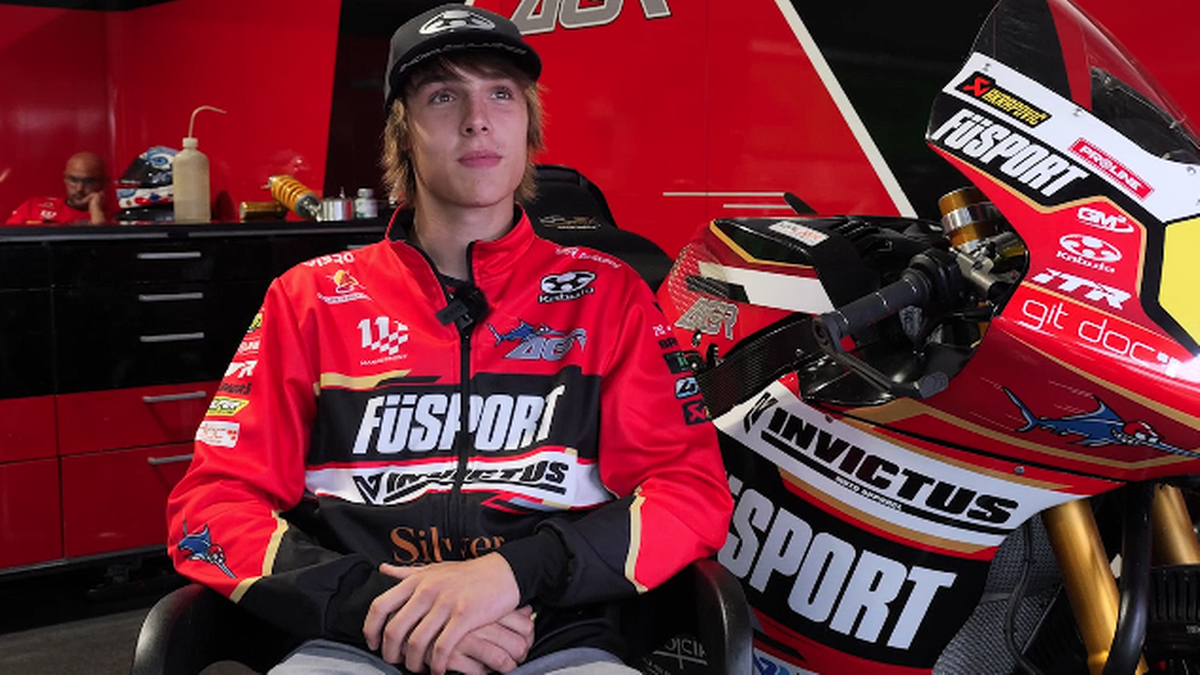 Młody motocyklista Milan Pawelec w czerwonej kurtce z logo ORLEN, siedzi obok motocykla.