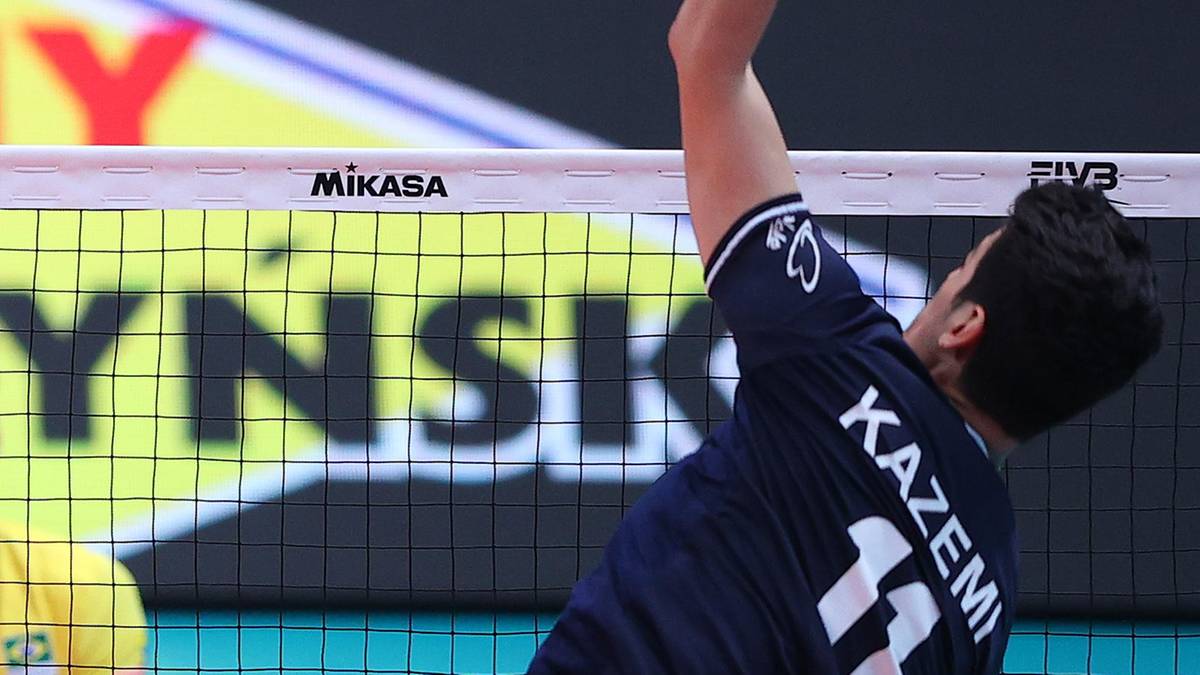 Siatkarz w granatowej koszulce z numerem 14 i nazwiskiem KAZEMI na plecach wykonuje akcję przy siatce.