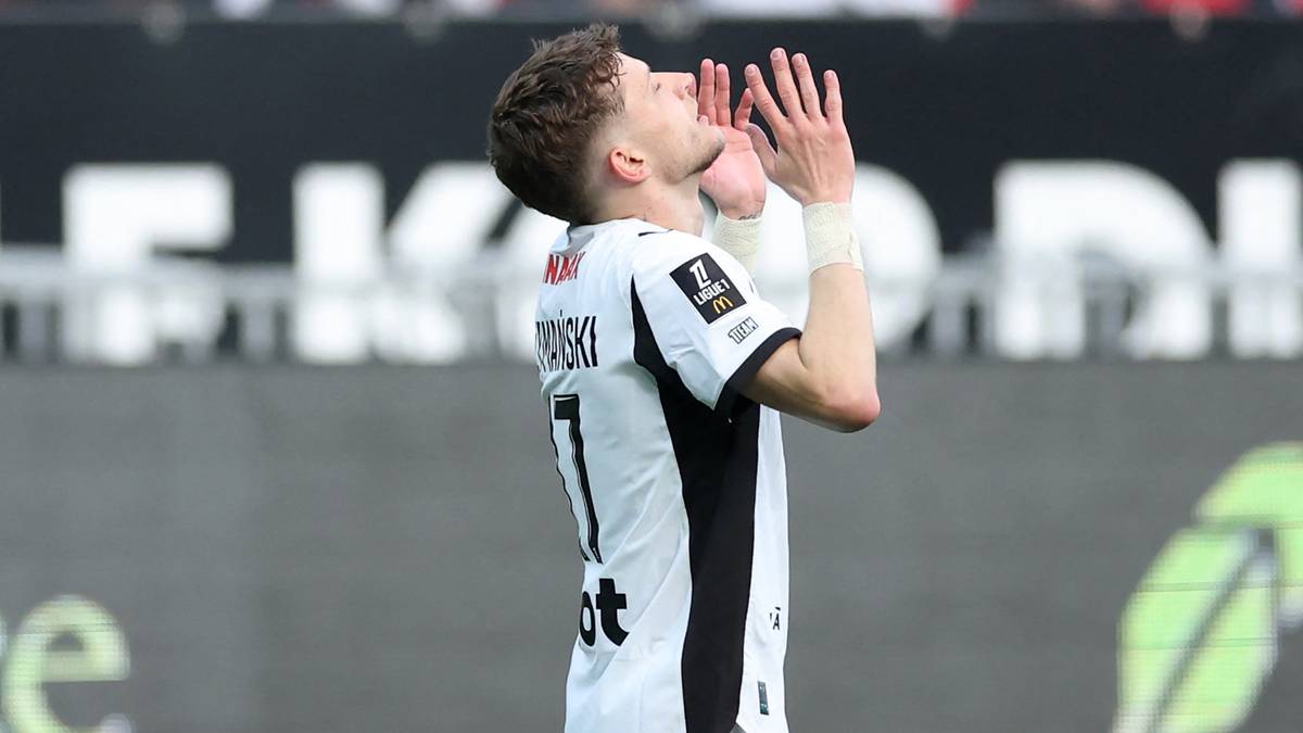 Piłkarz Sebastian Szymański klęczy na boisku z rękami złożonymi do g&oacute;ry, celebrując bramkę.