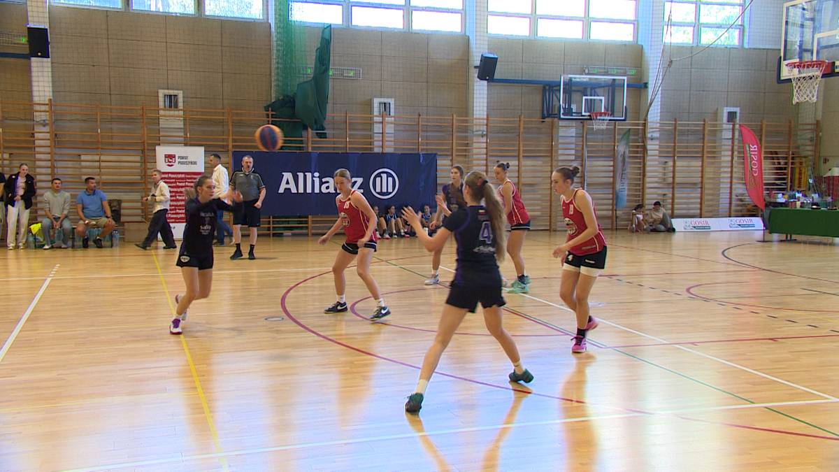 Dziewczęta grające w koszykówkę na boisku w hali sportowej, jedna z zawodniczek podaje piłkę do koleżanki z drużyny.
