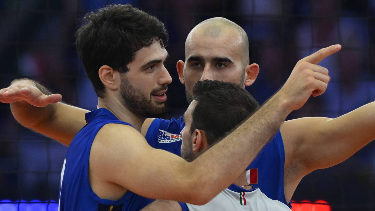 Trzech siatkarzy w strojach sportowych obejmuje się na boisku podczas meczu, jeden z nich ma numer 7 na plecach.