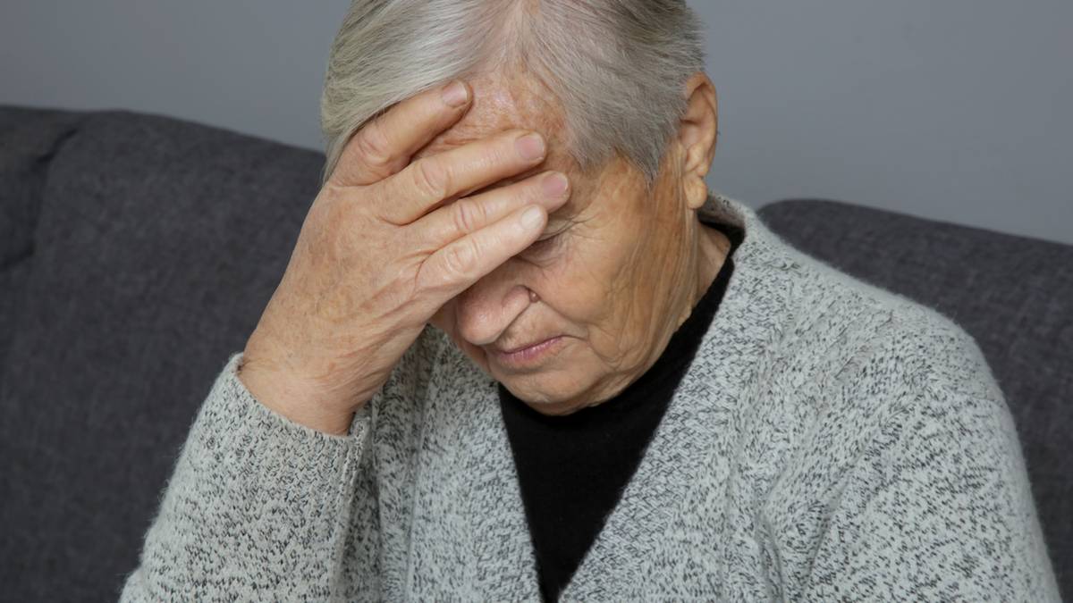 Starsza kobieta z ręką na czole, wyrażająca zmartwienie lub ból.