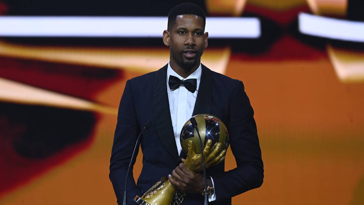 Wilfredo Leon, siatkarz w czarnym garniturze z muszką, trzyma złote trofeum w kształcie kuli ziemskiej.