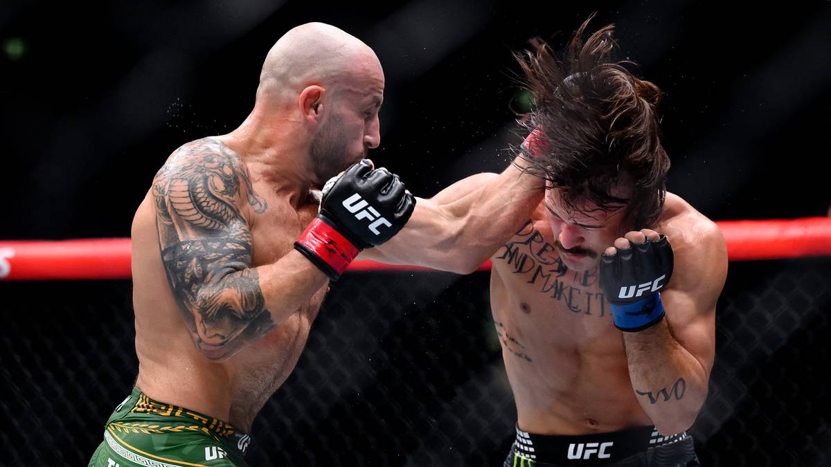 Dwóch zawodników MMA w akcji podczas walki. Jeden zawodnik w zielonych spodenkach zadaje cios.