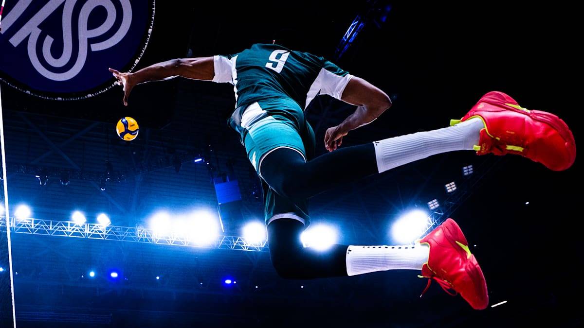 Zawodnik w skoku do uderzenia w piłkę do siatkówki, na ciemnym tle z niebieskimi światłami.