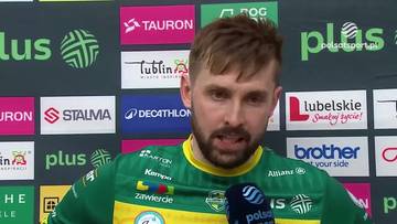 Portret mężczyzny z kr&oacute;tkimi, ciemnymi włosami i kilkudniowym zarostem, ubranego w zieloną koszulkę sportową z ż&oacute;łtymi elementami. Mężczyzna patrzy w obiektyw, trzymając mikrofon w dłoni.