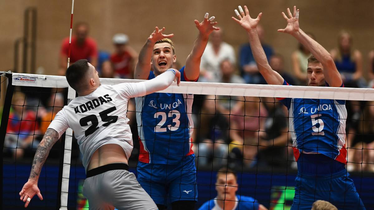 Siatkarze podczas meczu, jeden z nich o nazwisku Kordas na koszulce pr&oacute;buje zablokować atak przeciwnika przy siatce.