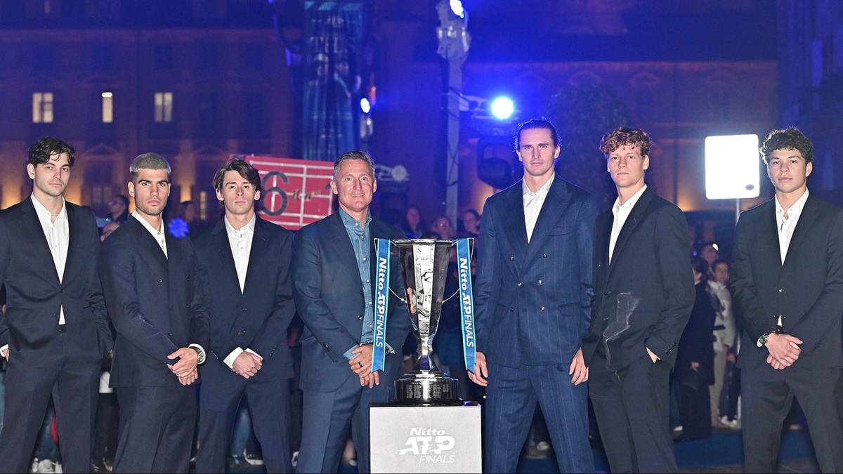 Grupa siedmiu tenisist&oacute;w w garniturach pozuje do zdjęcia z pucharem ATP Finals na tle tłumu.