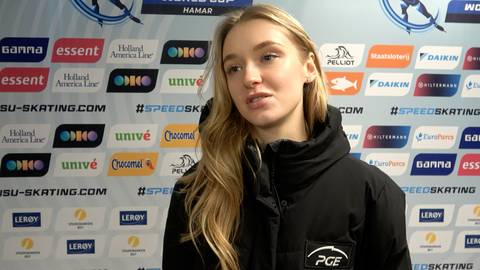 Martyna Baran, młoda kobieta o blond włosach, ubrana w czarną kurtkę, udziela wywiadu na tle ściany z logotypami sponsor&oacute;w.