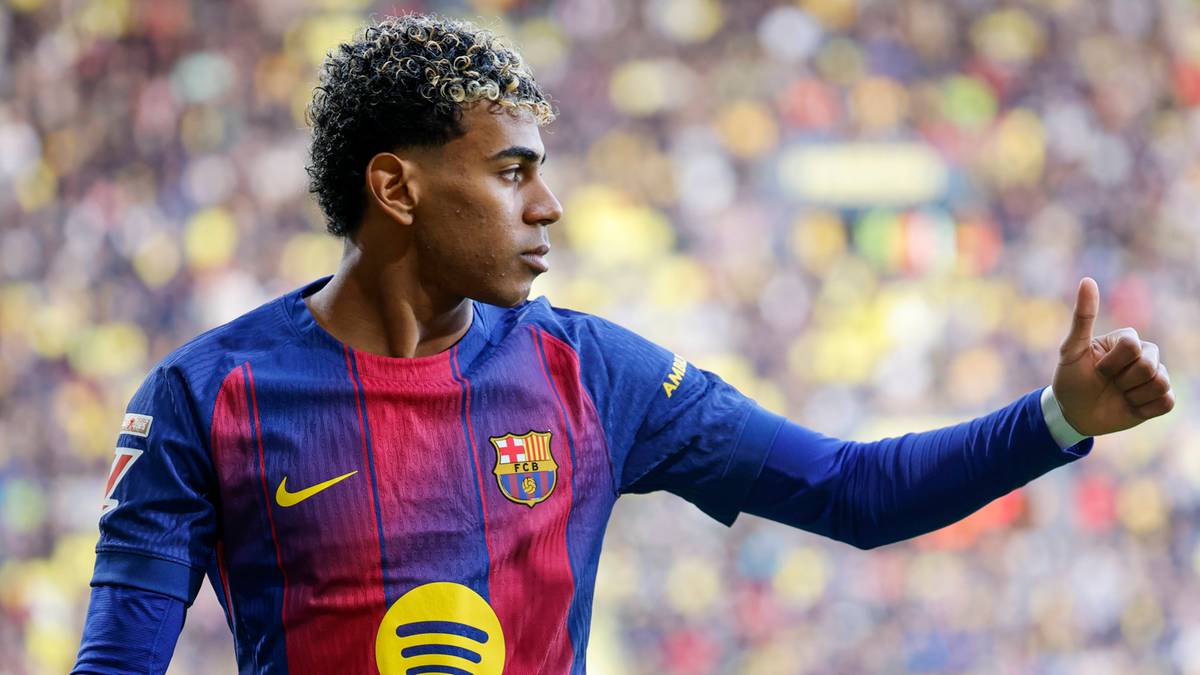 Młody piłkarz FC Barcelony z uniesionym kciukiem na tle trybun stadionu.