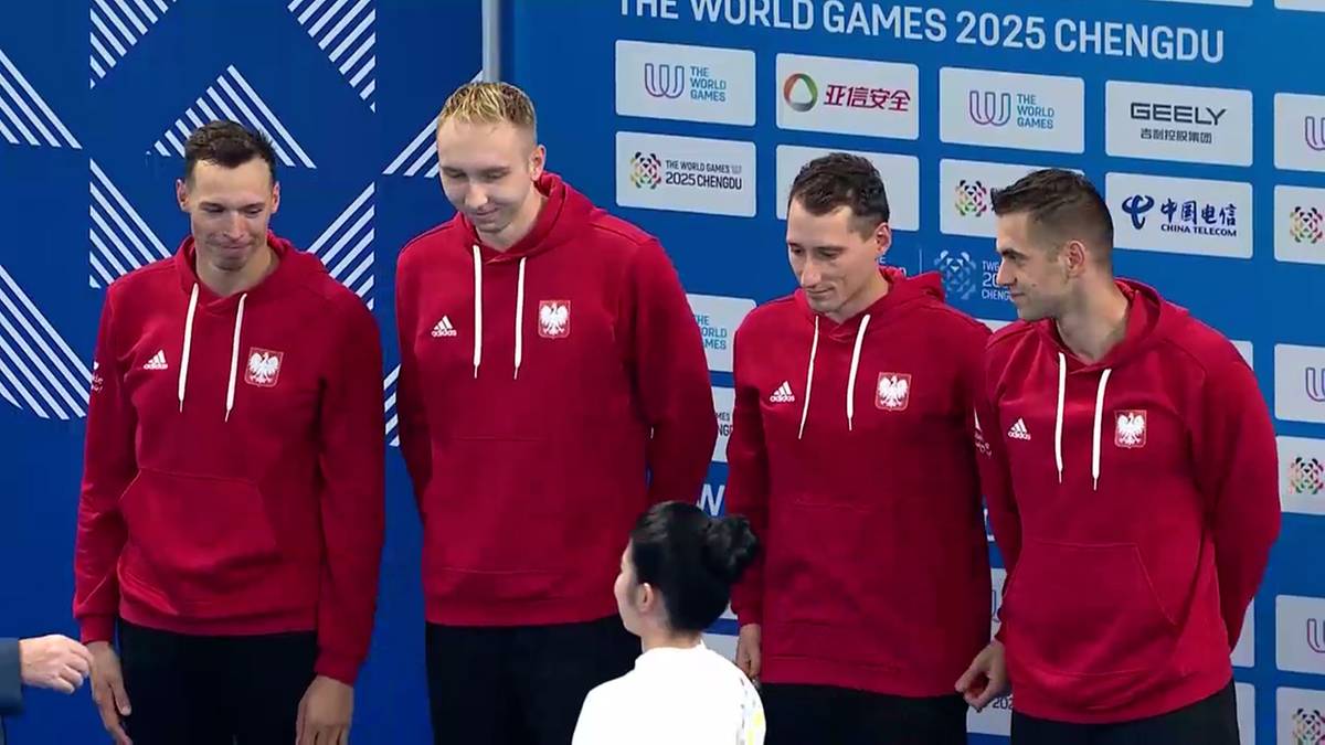 Czterech mężczyzn w czerwonych bluzach z orłem w koronie pozuje do zdjęcia.