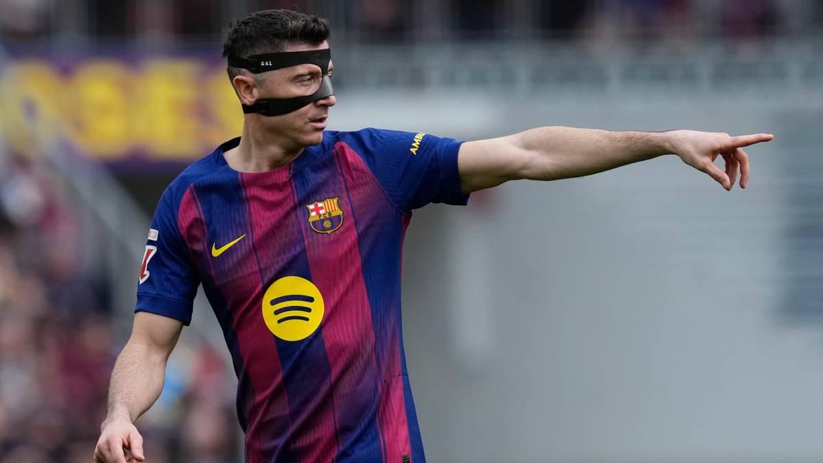 Piłkarz FC Barcelony Robert Lewandowski w koszulce klubowej z opaską na oku wskazuje palcem w bok.
