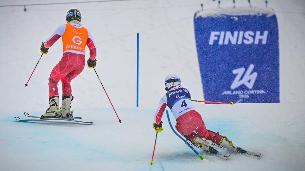 Dw&oacute;ch narciarzy w czerwonych kombinezonach na trasie zjazdowej, jeden z nich zbliża się do mety oznaczonej niebieską tablicą z napisem "FINISH".