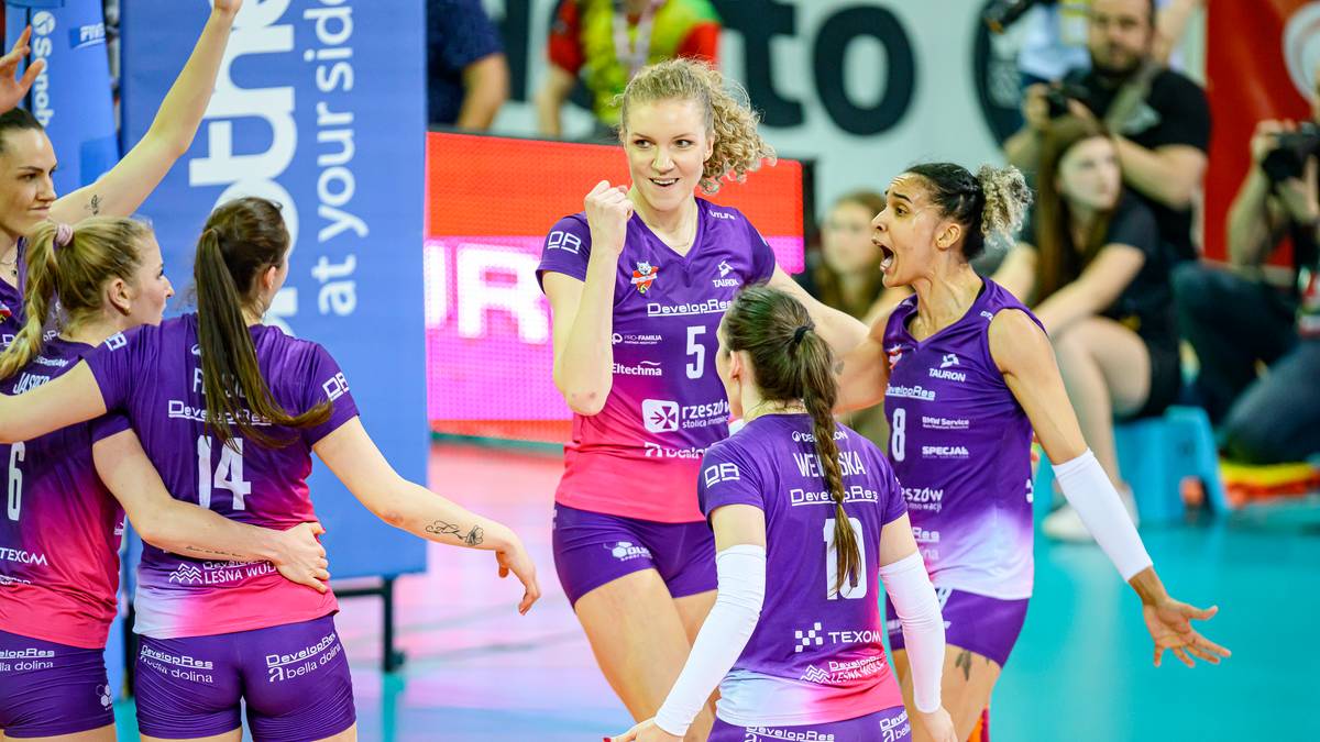 Grupa siatkarek w fioletowych strojach świętuje zwycięstwo, jedna z nich unosi pięść w geście radości.