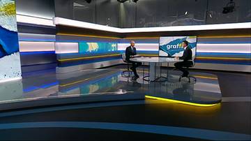 Dwaj mężczyźni w garniturach siedzący przy okrągłym stole w nowoczesnym studiu telewizyjnym.