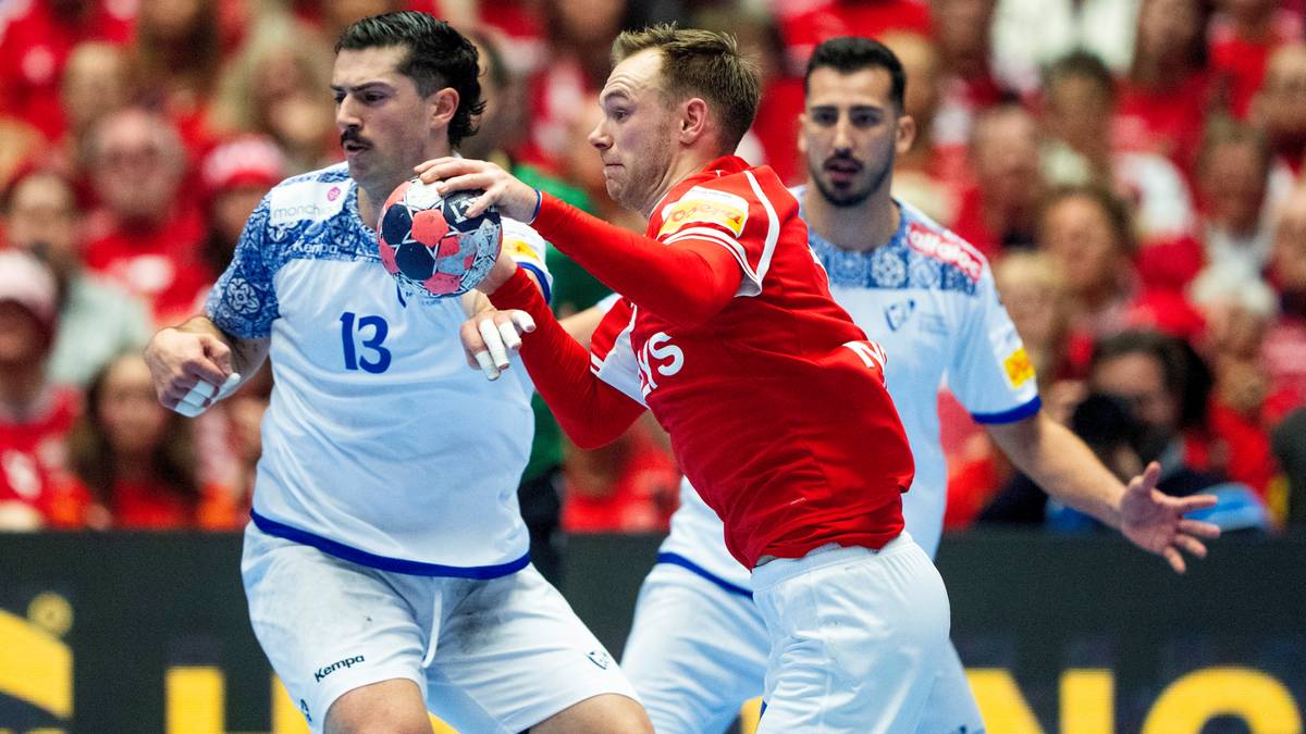 Piłkarze ręczni w akcji, jeden w czerwonej koszulce pr&oacute;buje odebrać piłkę zawodnikowi w białej koszulce z numerem 13.