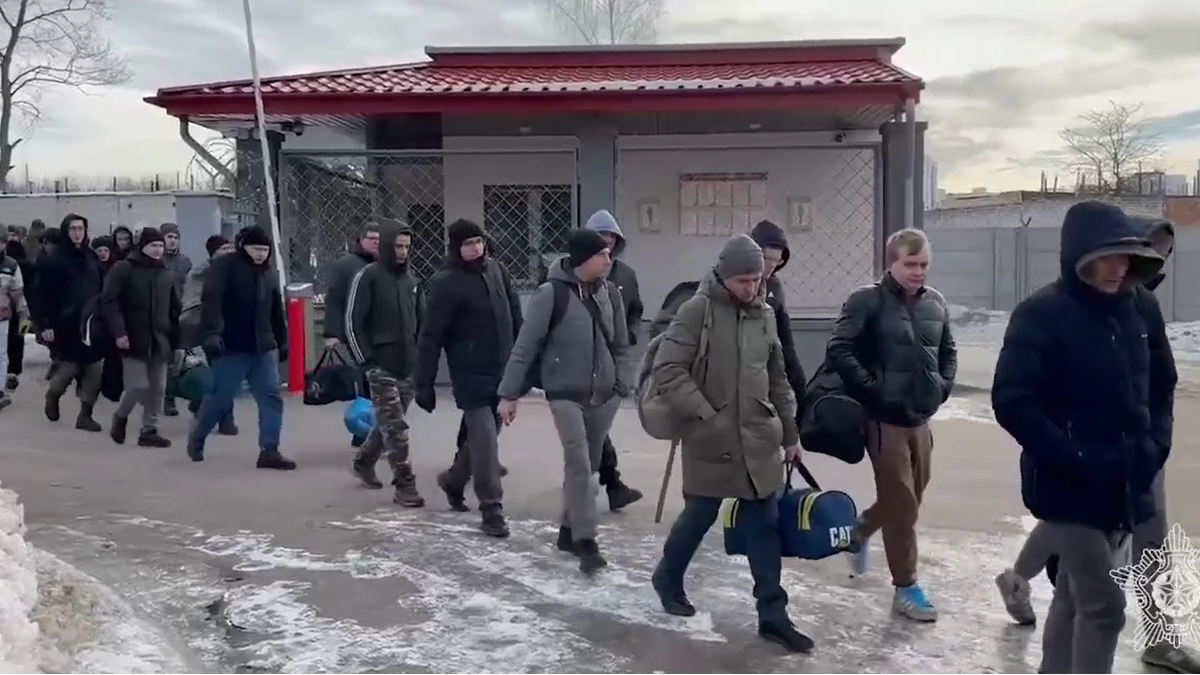 Grupa mężczyzn z torbami idzie w stronę bramy.