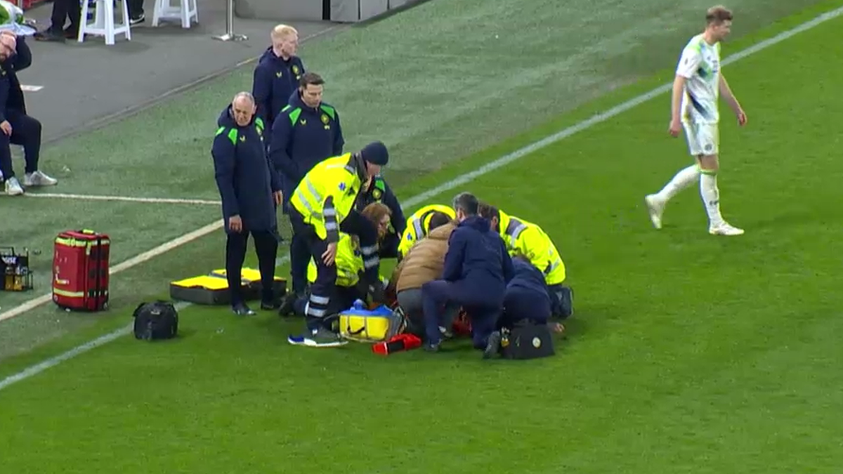 Personel medyczny udziela pomocy leżącemu zawodnikowi na boisku podczas meczu piłki nożnej.