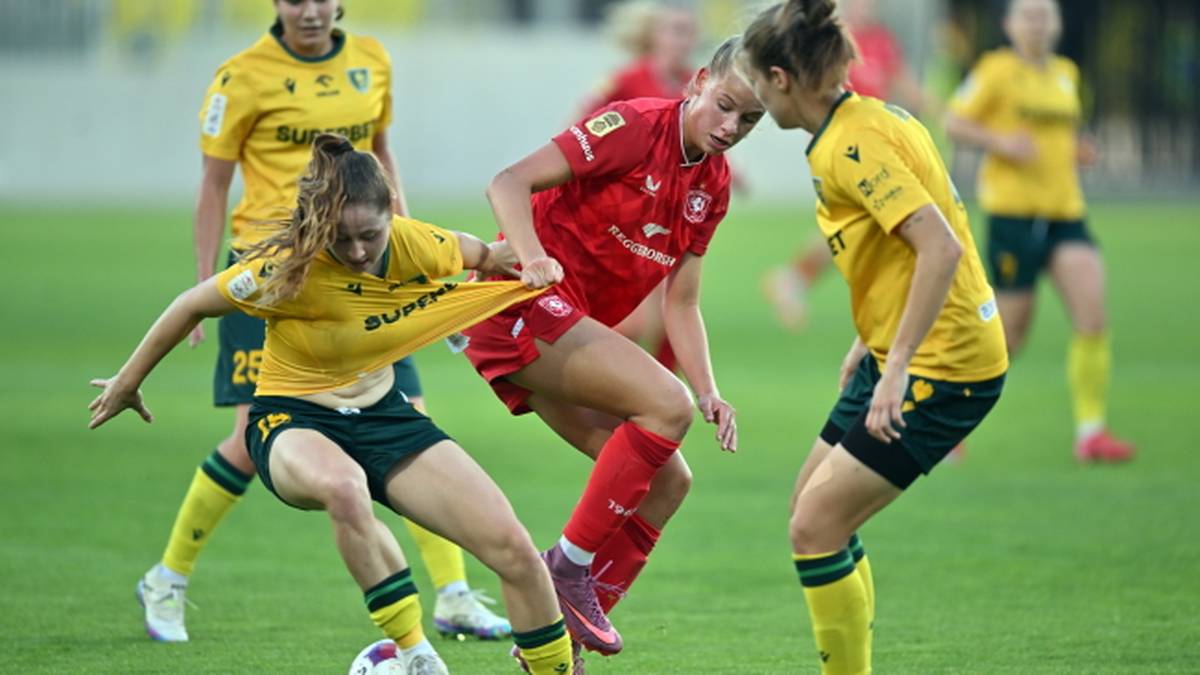 Piłkarki w zielonych i czerwonych strojach walczą o piłkę nożną na boisku.