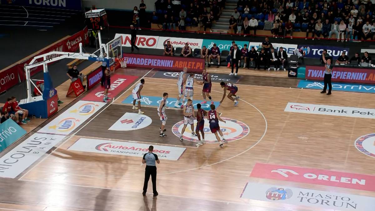 Drużyna koszykarzy w czerwonych strojach atakuje kosz przeciwnej drużyny na drewnianym boisku.