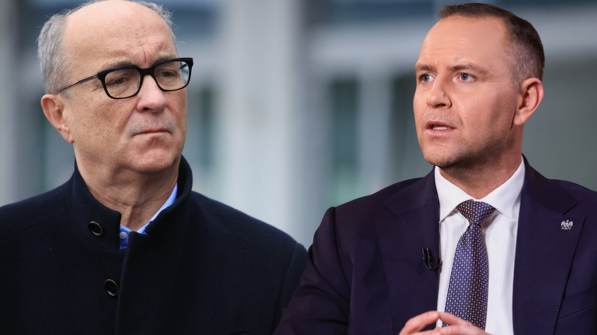 Dw&oacute;ch mężczyzn w garniturach, jeden starszy z okularami, drugi młodszy, siedzi w tle rozmytego biurowca.