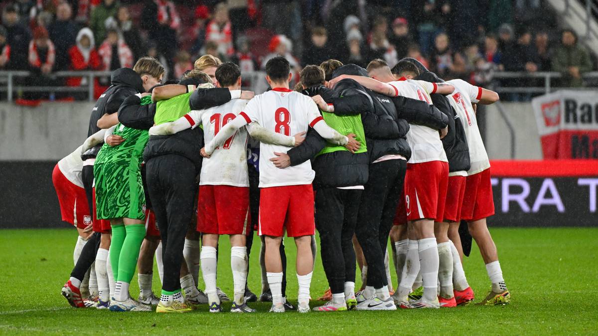 Piłkarze reprezentacji Polski do lat 21 stoją w kółku na boisku, przytulając się, świętując zwycięstwo.