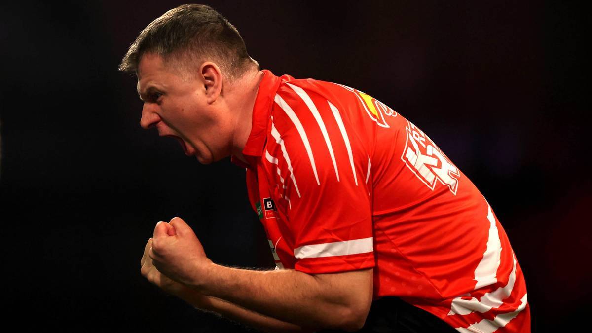 Mężczyzna w czerwonej koszulce sportowej z zaciśniętymi pięściami i ekspresyjną miną.