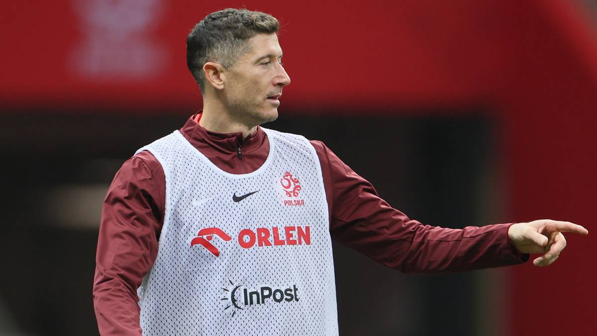 Piłkarz reprezentacji Polski w białej kamizelce treningowej wskazuje palcem w bok.