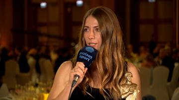 Kobieta z długimi brązowymi włosami trzyma mikrofon z logo Polsat Sport i nagrodę w kształcie statuetki.