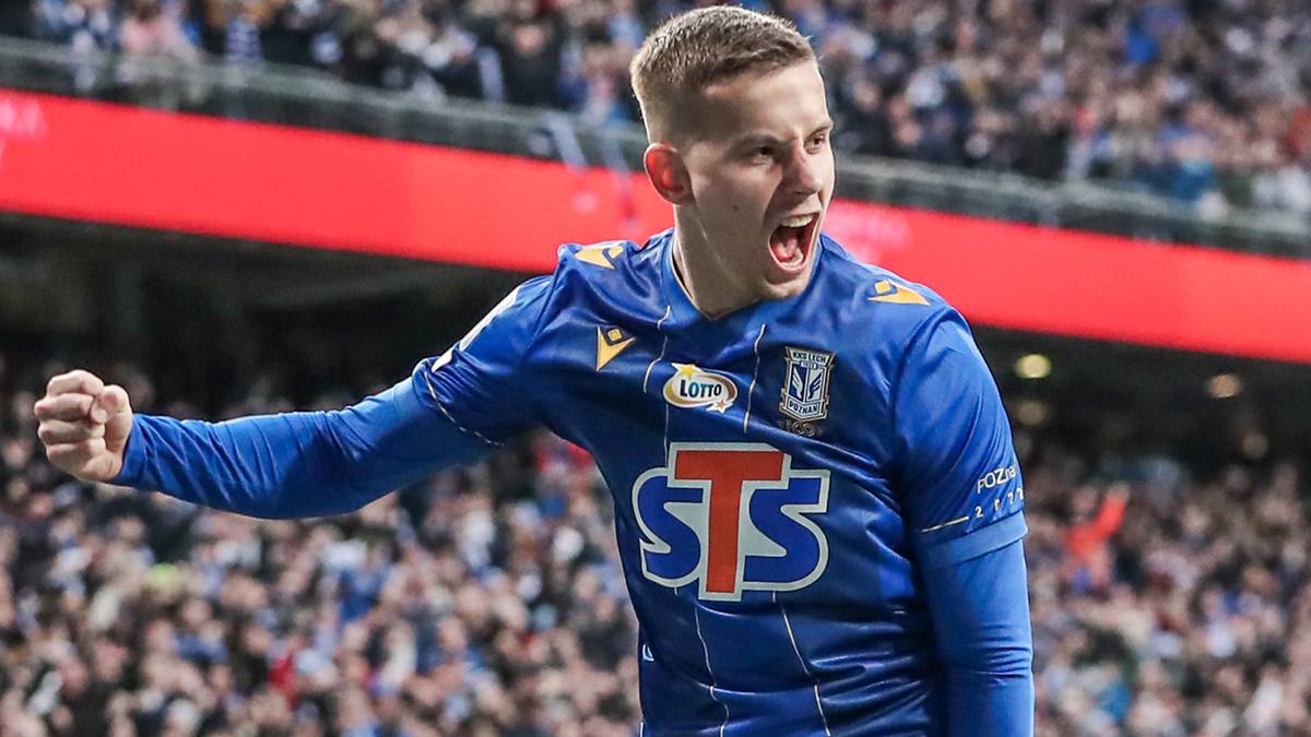 Piłkarz w niebieskiej koszulce z widocznym napisem STS świętuje zdobycie gola, z zaciśniętą pięścią i otwartymi ustami.