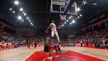 Zawodnik wykonuje efektowny wsad do kosza, znajdując się w powietrzu.