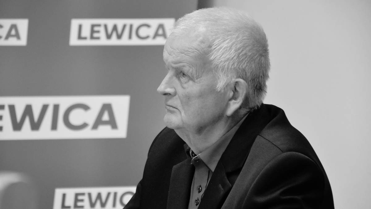 Starszy mężczyzna, radny Jan Pszczoła, siedzi na tle logo Lewicy.