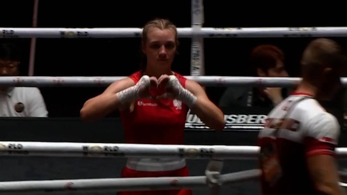 Bokserka w czerwonym stroju z rękami złożonymi w kształt serca na tle ringu.