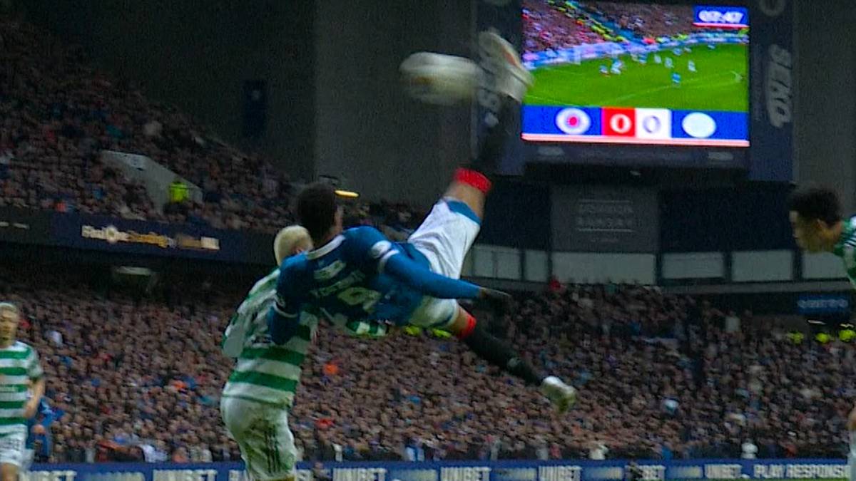 Piłkarz wykonuje przewrotkę podczas meczu piłki nożnej, pr&oacute;bując strzelić gola. W tle widoczni inni zawodnicy i trybuny kibic&oacute;w.