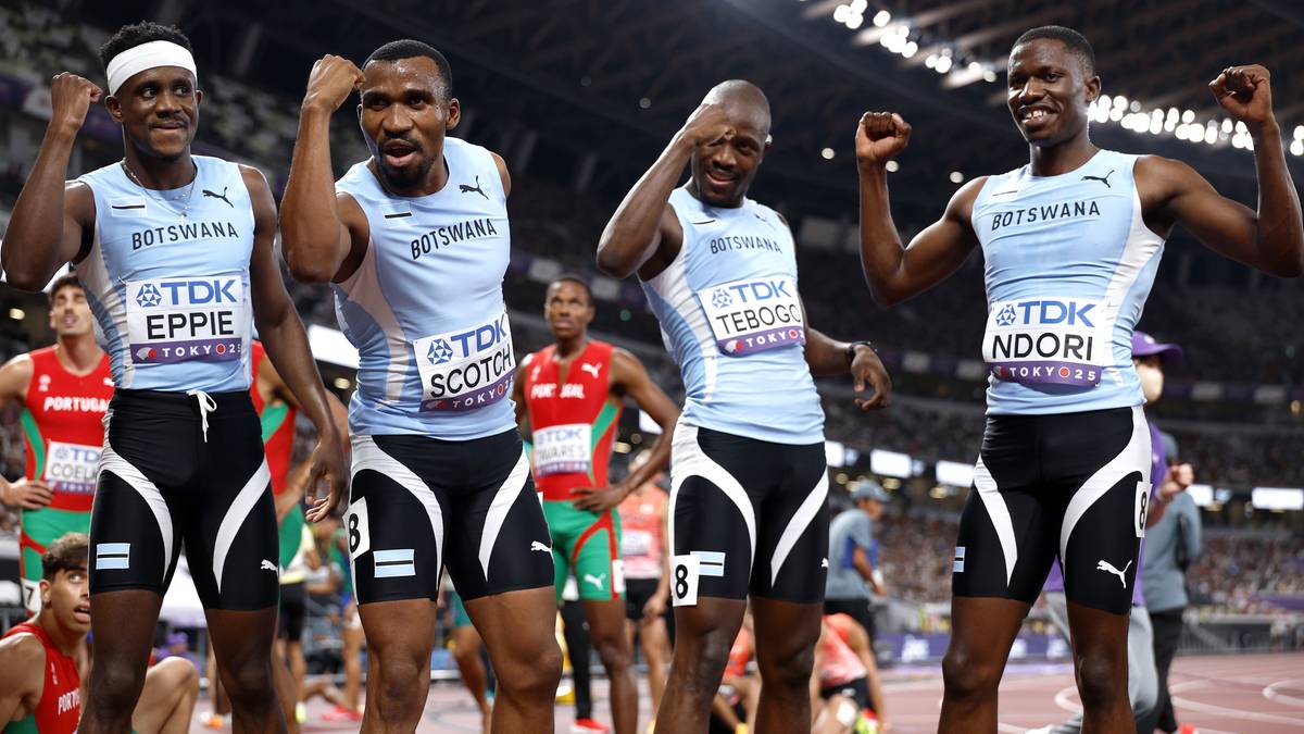 Czterech lekkoatletów w jasnoniebieskich koszulkach i czarnych spodenkach z białymi paskami świętuje zwycięstwo w sztafecie. Ich nazwy to "EPPIE", "SCOTO", "TEBOGO" i "NDORI". Wszyscy unoszą ręce w geście triumfu na tle stadionu.