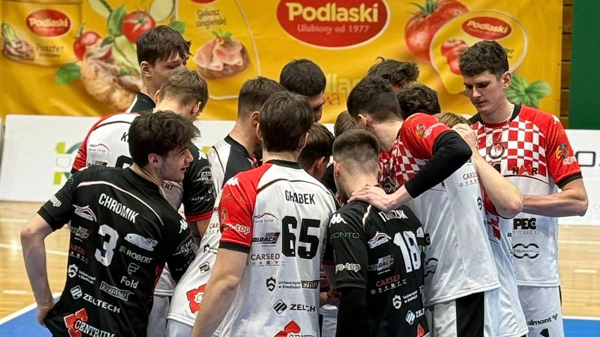 Grupa młodych siatkarzy w strojach sportowych stoi w k&oacute;łku, omawiając strategię.