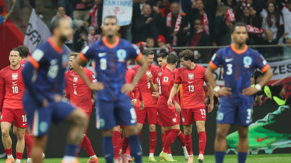 Piłkarze w czerwonych strojach na boisku, w tle kibice na trybunach.