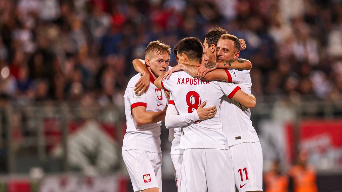 Piłkarze reprezentacji Polski w białych strojach przytulają się na boisku.