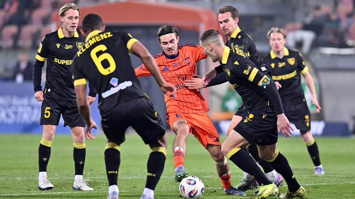 Gracze dwóch drużyn piłkarskich rywalizują o piłkę na zielonym boisku.