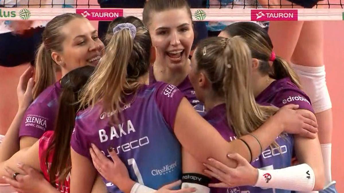 Siatkarki w fioletowych strojach świętują zwycięstwo, przytulając się.