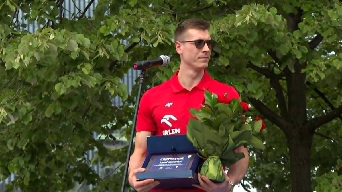 Kamil Semeniuk odbiera wyr&oacute;żnienie, trzymając bukiet kwiat&oacute;w i pudełko z dyplomem.