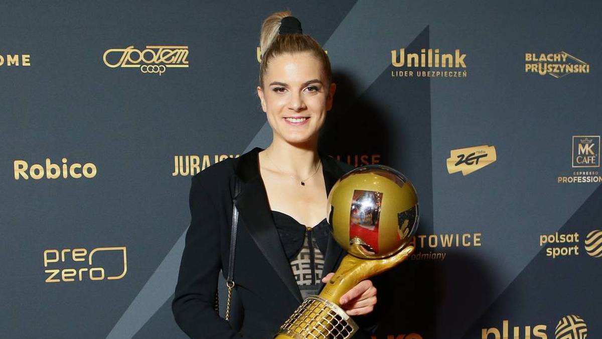 Uśmiechnięta kobieta w eleganckim czarnym stroju trzymająca złote trofeum.