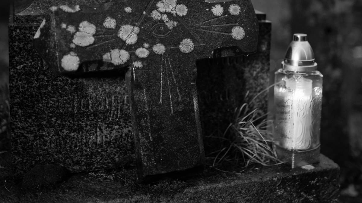 Fragment nagrobka z zapalonym zniczem na cmentarzu.