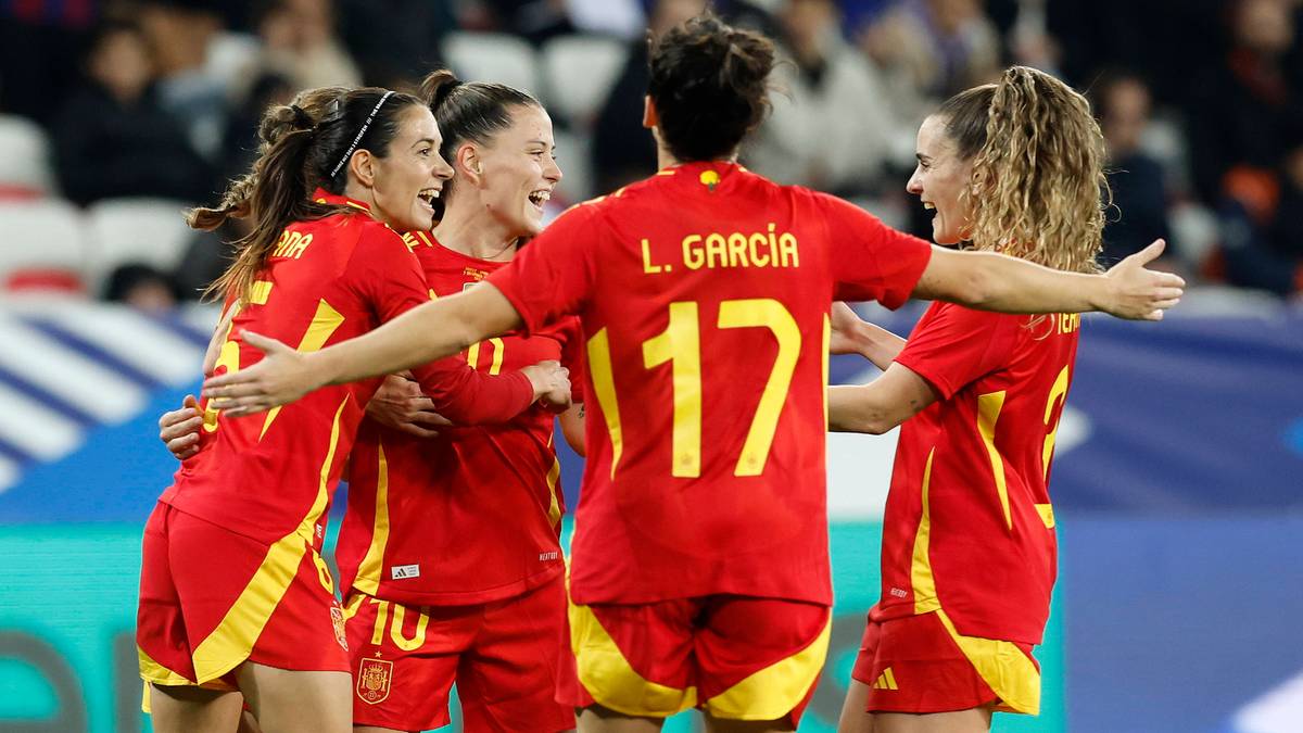 Cztery piłkarki nożne w czerwonych strojach z żółtymi detalami, cieszące się po zdobyciu gola. Jedna z zawodniczek ma na plecach numer 17 i nazwisko L. GARCIA. Ich ramiona są splecione na sobie w geście radości.