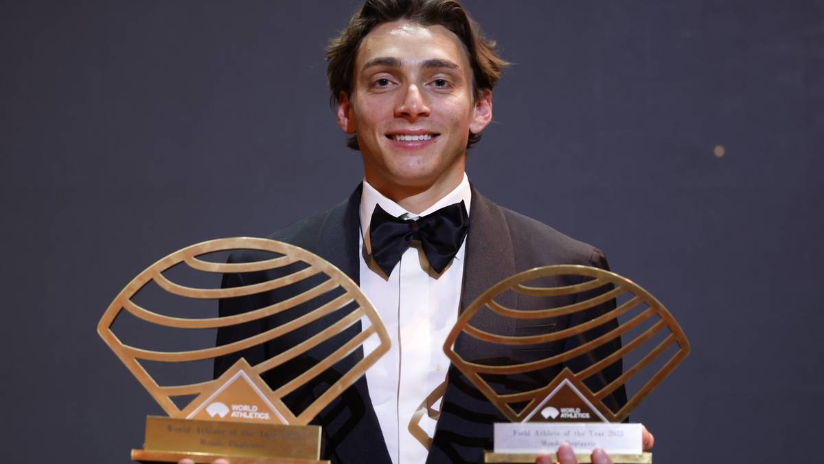 Młody mężczyzna w eleganckim stroju trzyma dwie złote nagrody w kształcie wachlarza.