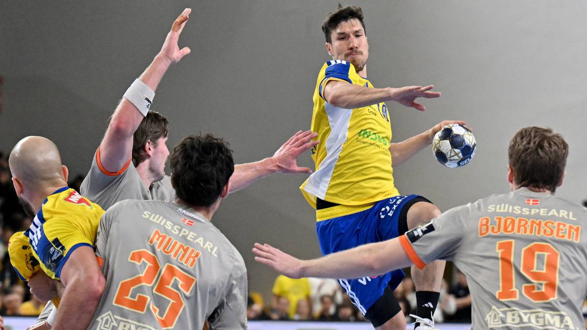 Gracz Industrii Kielce w żółtej koszulce rzuca piłkę do bramki, otoczony przez zawodników Aalborg HB.